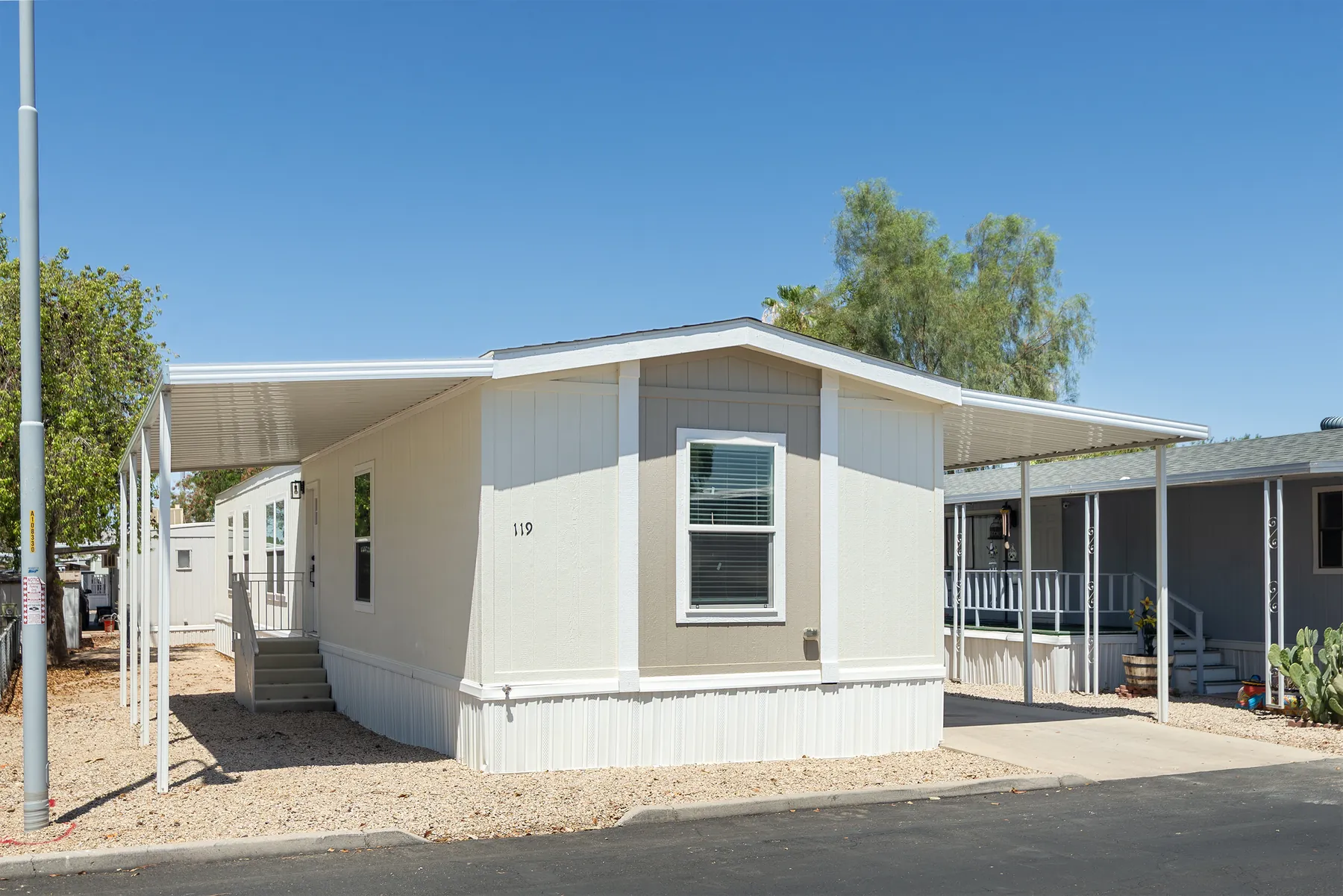 Home #119: gray single-wide with white trim, entry steps and covered carport