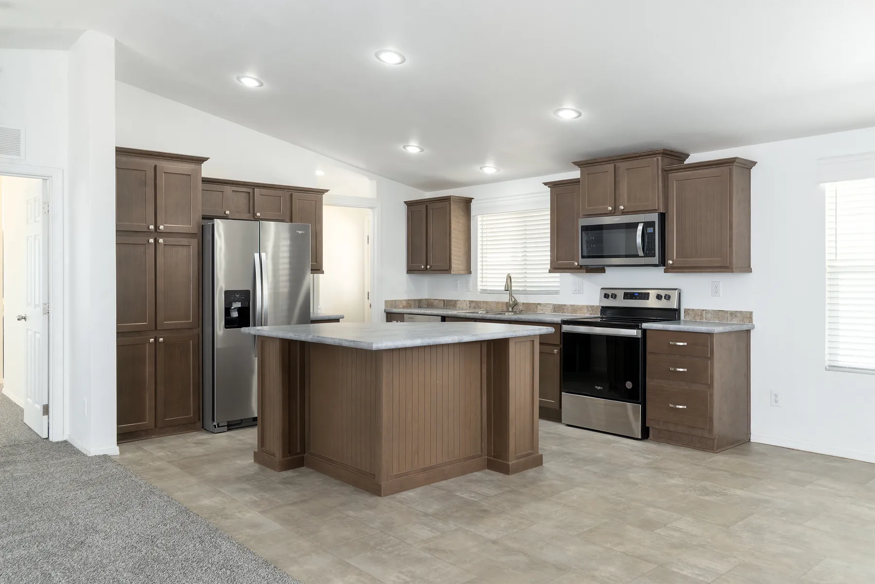 Island kitchen with pantry cabinets and stainless appliances in home #70, a double-wide for sale at Paradise Groves