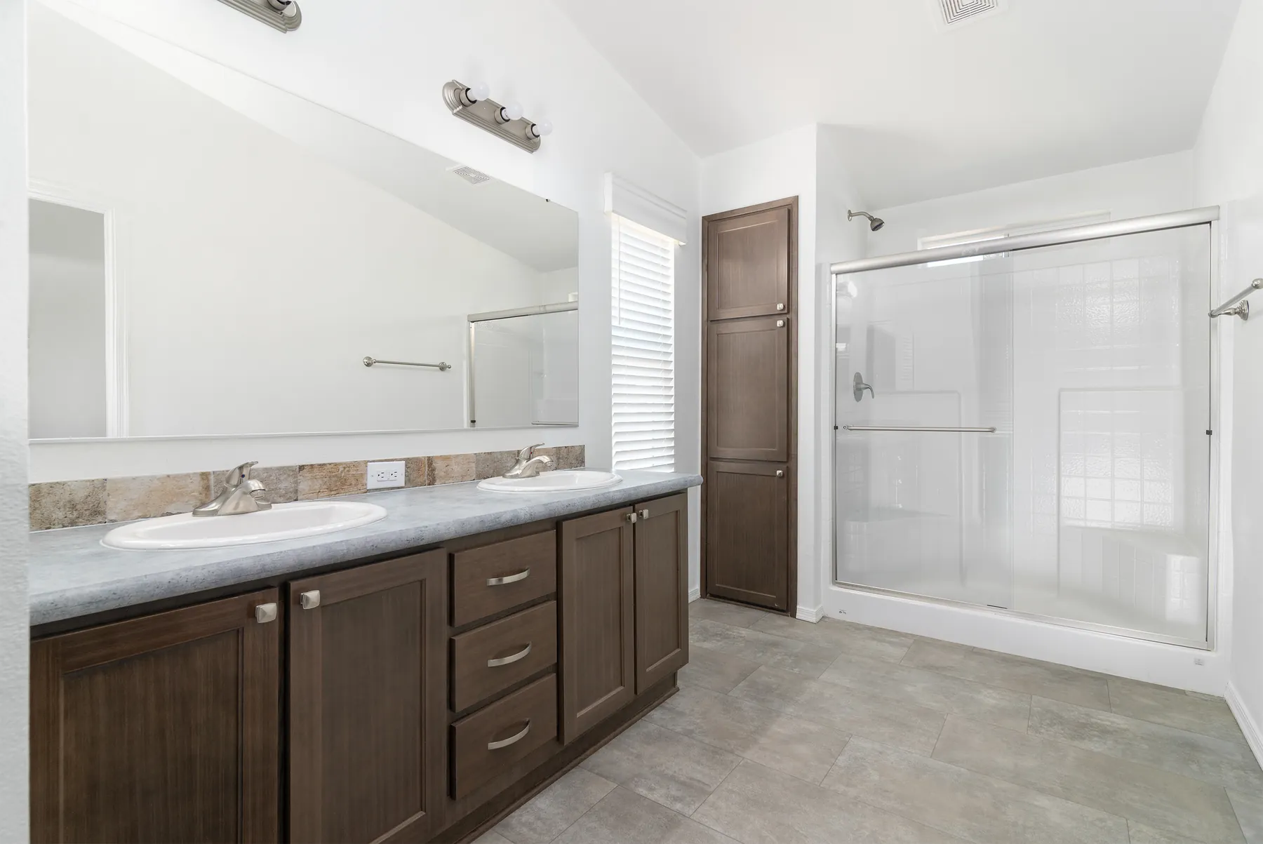 Primary bathroom with double vanity, linen cabinet and glass shower
